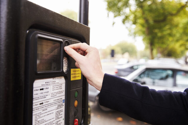 Close Up Of Man Putting Money In Parking Meter For Ticket.