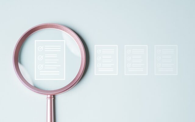 Document evaluation inspect. Contract agreement audit. Assessment survey evaluation check. A magnifying glass is used to look at a series of papers with check marks on them.