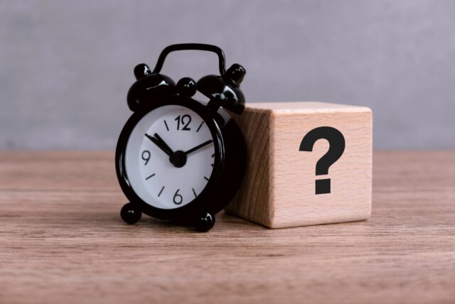 Wooden Cube with Question Mark Symbol with alam clock on wooden table.
