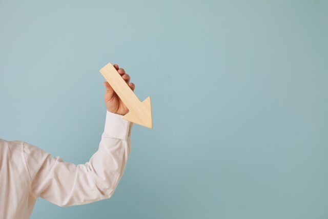 Man holding graph chart arrow that's pointing down on blue blank background.