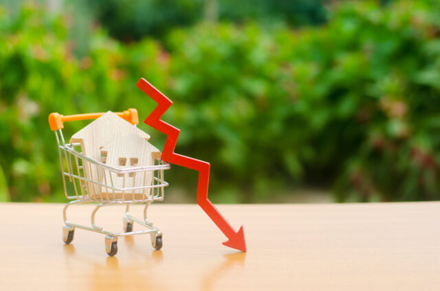 Two wooden houses in a trading cart and red arrow down, representing loss of investment in commercial properties.