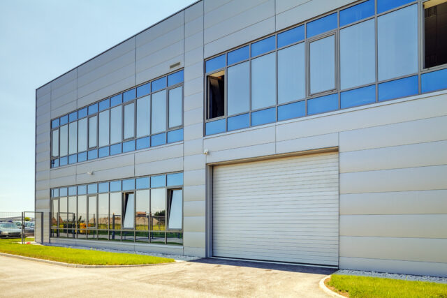 A picture of a grey facade made of aluminum panels with doors and windows on industrial /commercial building.