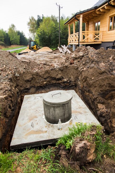 A construction shot of a septic tank being installed or assessed in a countryside garden.