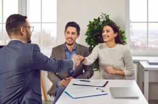 Happy couple shaking hands with a male solicitor. Cheerful young man and woman having a good professional neglgeince consultation with their solicitor sitting in the office.