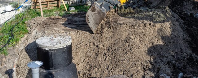 Using an excavator to bury a 10 m3 concrete septic tank located in the garden next to the house.