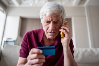 Trusting serious, feared pensioner giving away card number to fraudsters over phone. Financial scam, bank card fraud representing APP and bank transfer scams.