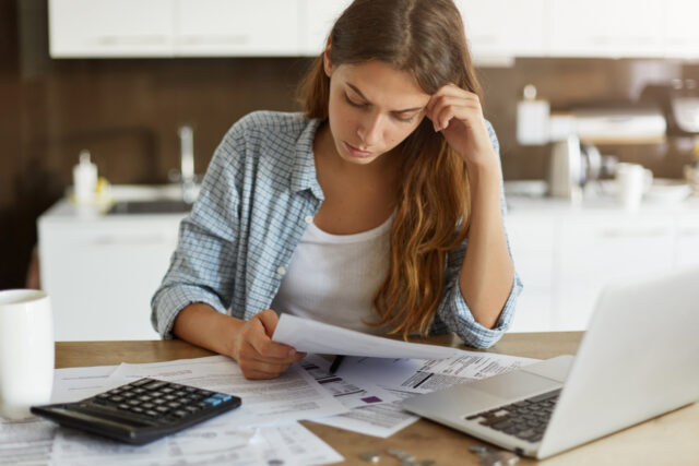 Frustrated person reviewing financial paperwork with calculator on desk