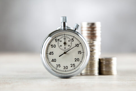 Analog stopwatch with a stack of coins in the background symbolising urgency in scam recovery claims.