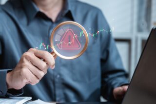 A man is holding a magnifying glass over a computer screen with a red warning sign for mis-sold investments.