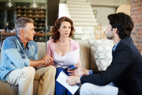 Mature couple reviewing complex financial documents with an adviser highlighting potential mis-sold investment risks.